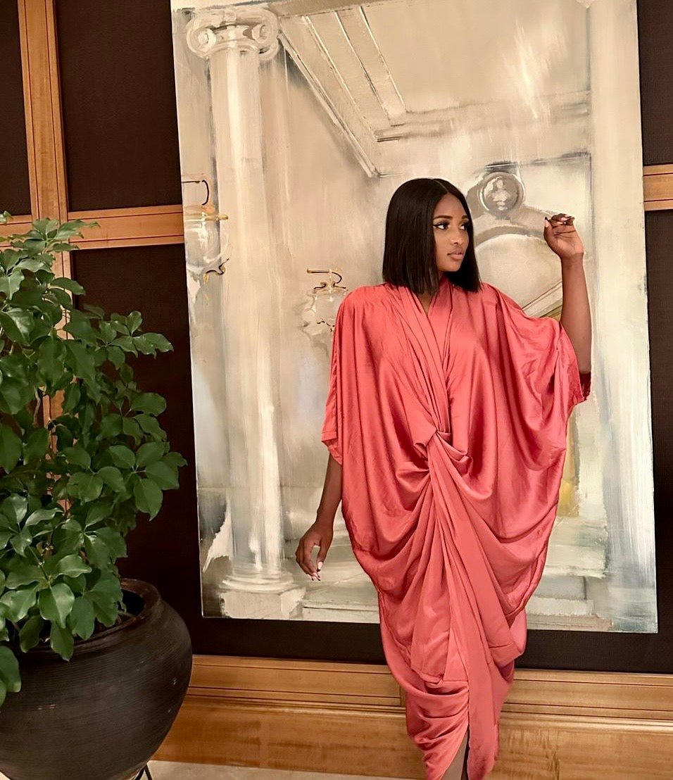 A woman models the bibianna.co.uk Silk Dress, standing before a large classical painting with one hand raised; a potted plant appears on the left.