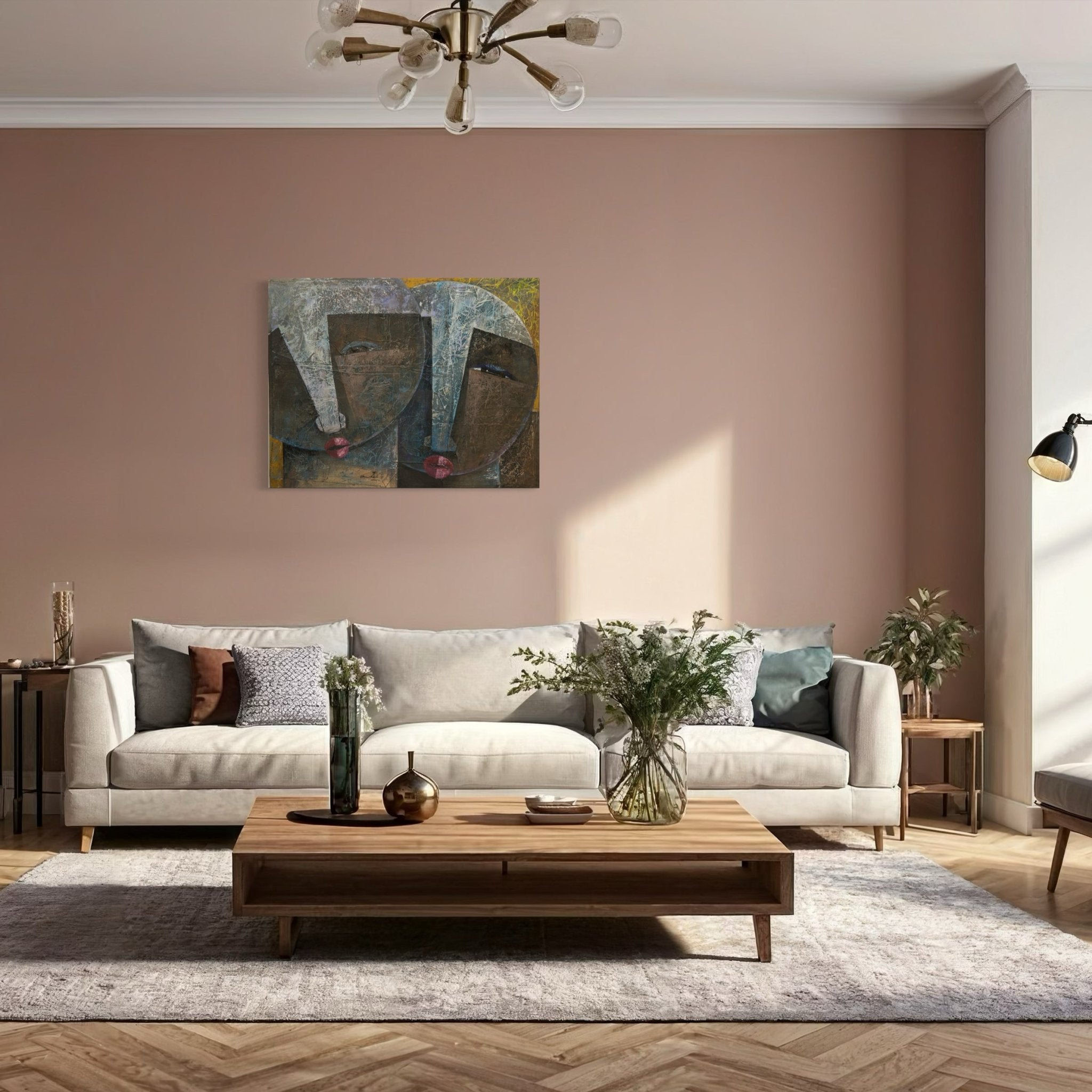A modern living room with a beige sofa, wooden coffee table, plants, and Christopher Ankeli’s "Abstract Faces Collage Painting: Sour Ties" on a pink accent wall, brightened by natural light and a brass chandelier.