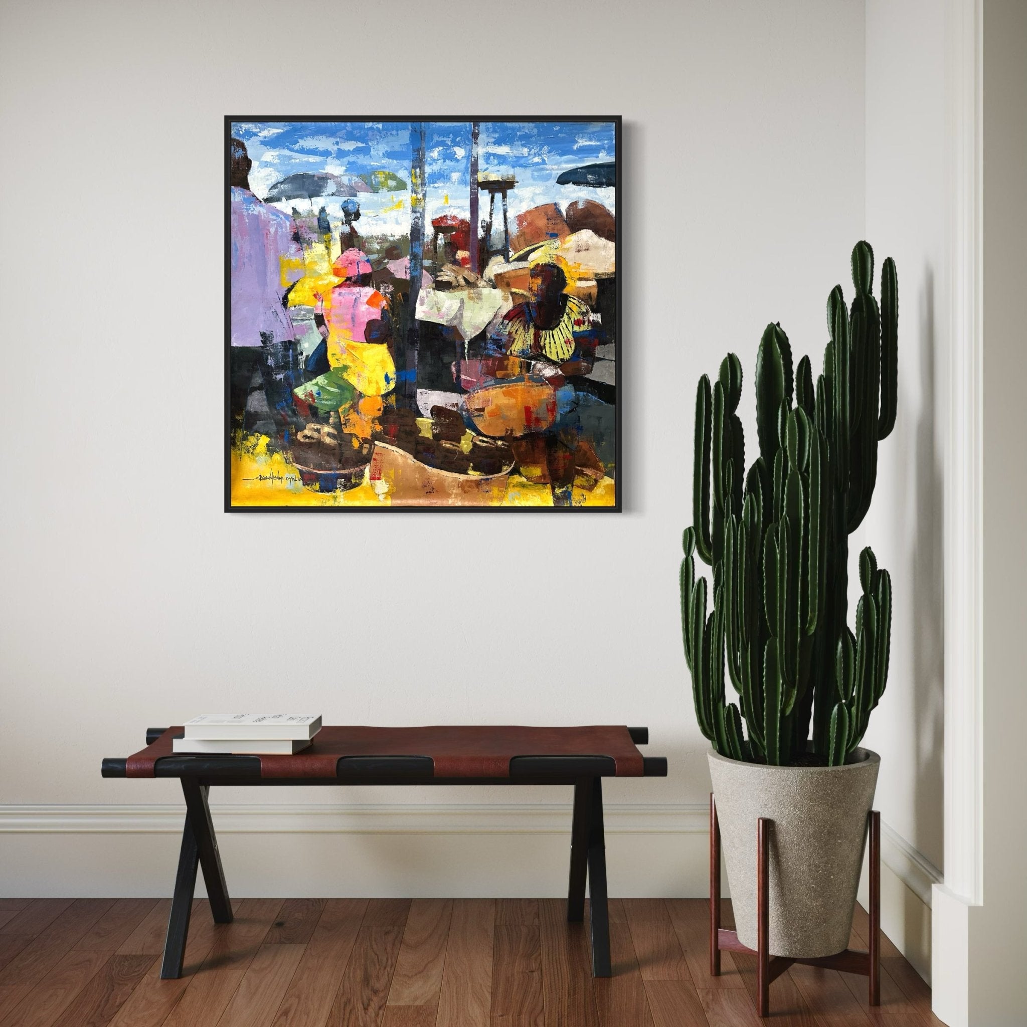 A framed, hand-signed "Stockfish" Contemporary Colourful Abstract Market Scene by Olasunkanmi Oyelusi decorates a minimalist room with a wooden bench, books, and cactus. Includes certificate of authenticity for this unique artwork.