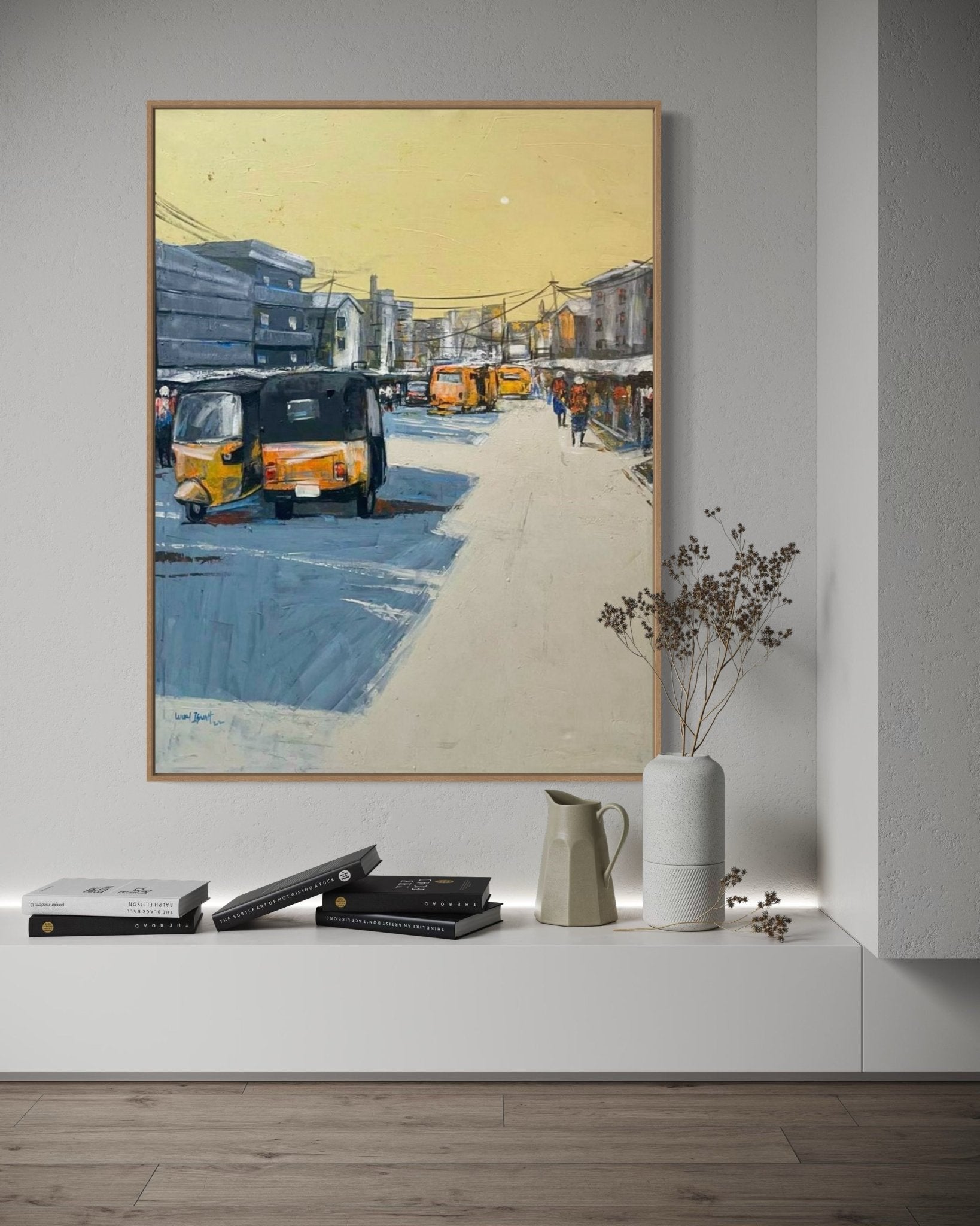 Streets Of Lagos" by Lucky Isaiah: a framed original painting of a sunny urban street with yellow auto rickshaws and people, displayed above a minimalist shelf. Includes certificate of authenticity.