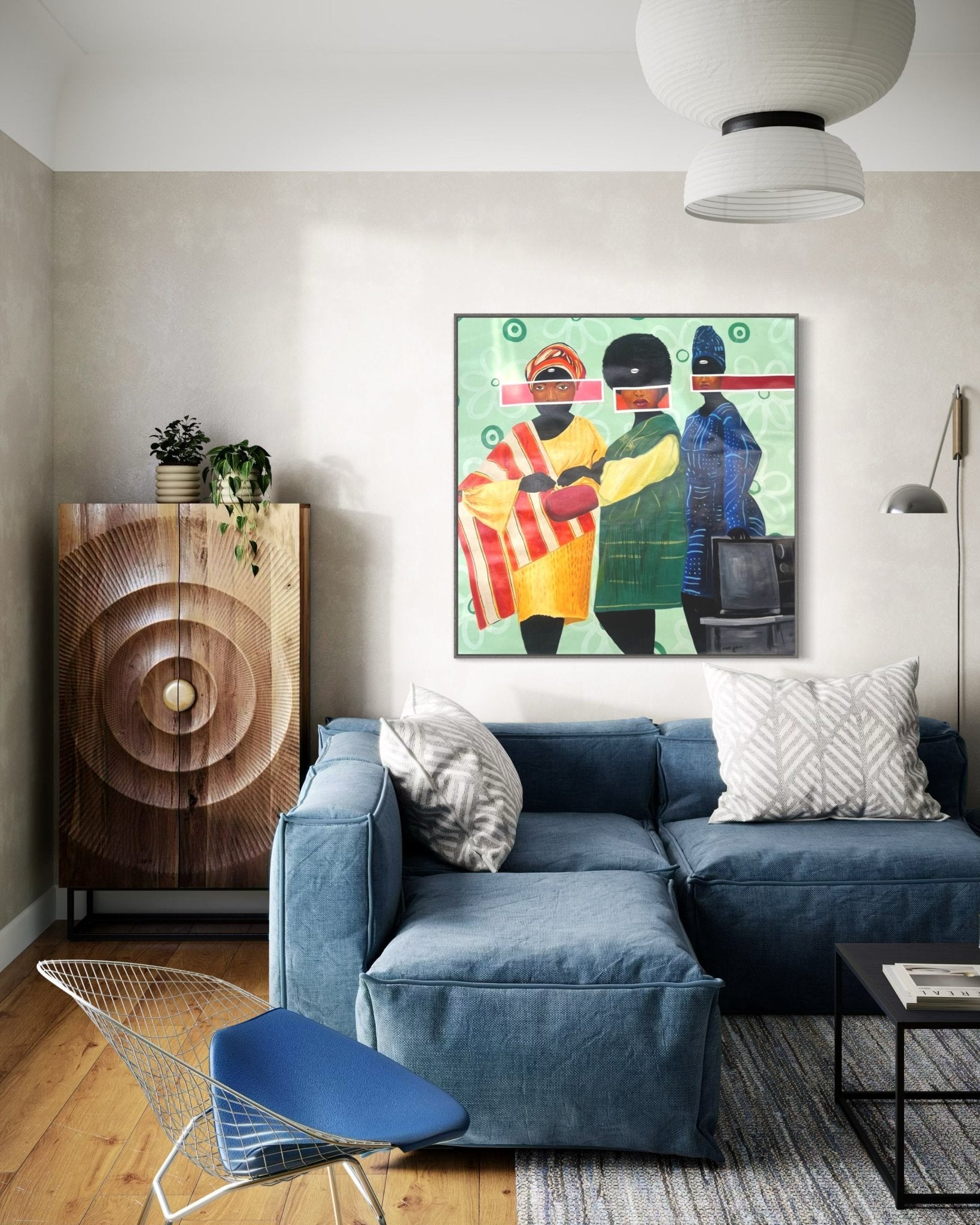 A modern living room features Afuope Opeyemi’s "Sunday Best" art, a blue sectional, patterned pillows, geometric wood cabinet with a plant, wire chair, hanging lamp, abstract acrylic-on-canvas wall art, and wood flooring.