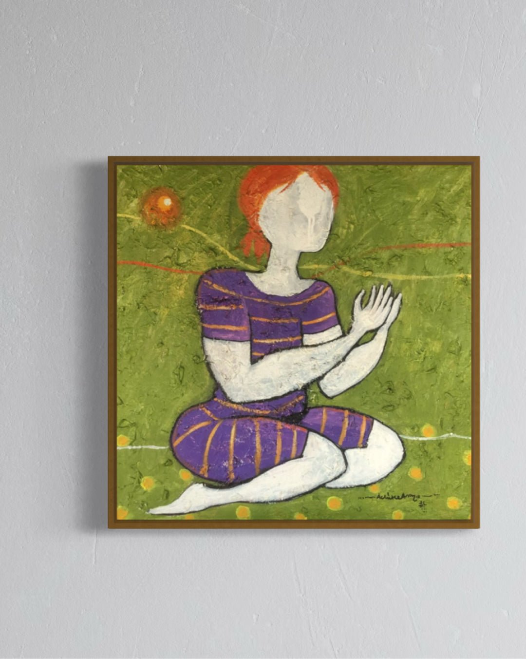 Suplication 4" by Achike Anayo is an acrylic on canvas painting of a faceless figure with red hair kneeling on grass in a striped outfit, hands together, before a glowing orange sun. Displayed framed on a gray wall.