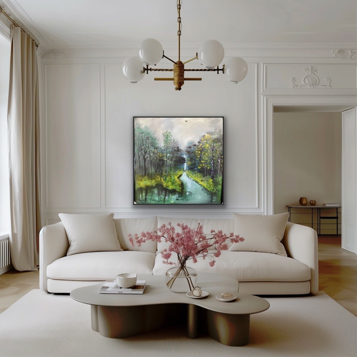 A modern living room features a white sofa, beige rug, and coffee table with pink flowers. Above the sofa hangs "The Great Outdoors" by Oyebisi Elijah, a hand-signed acrylic on canvas. A chandelier completes the elegant space.