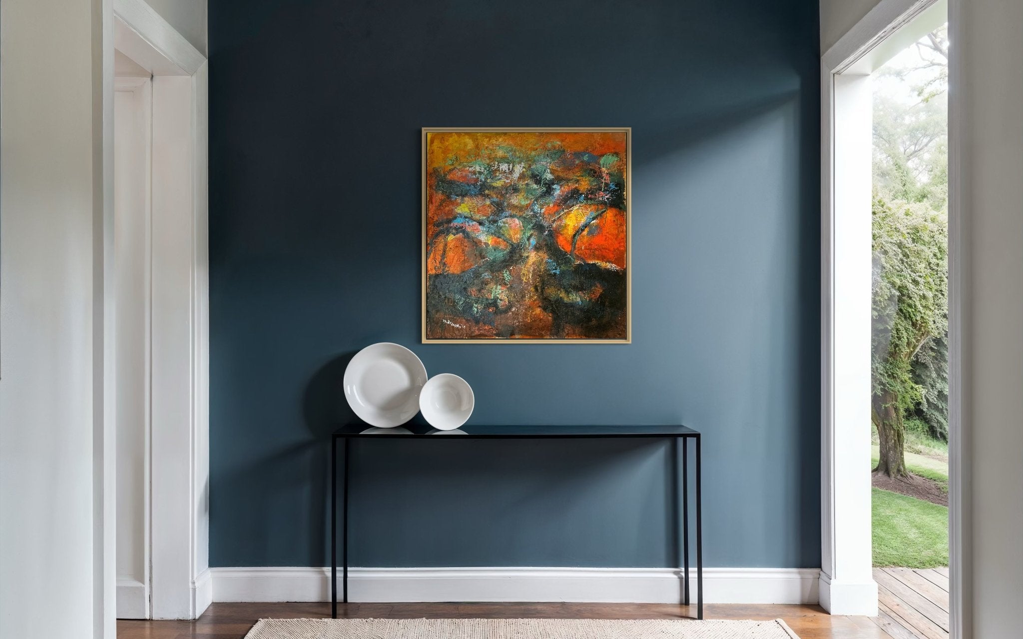 A modern hallway with dark blue walls features “Tree Of Life” by Bibianna African Art Collective, a hand-signed abstract painting. A black console table and three white bowls complete the space as sunlight reveals greenery outside.