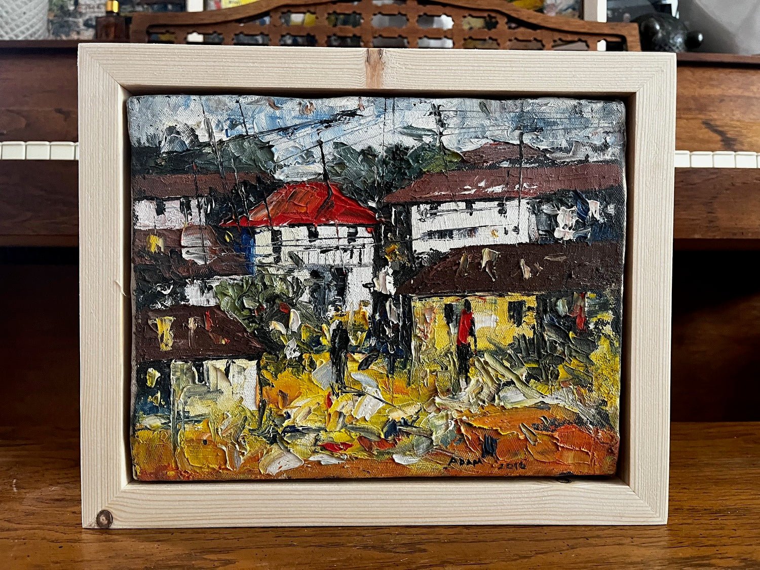 The "Lagos Streets" miniature acrylic on canvas by Adam features heavily textured impressionist scenes of houses and people, blending vibrant yellow, brown, and green hues with red and white roofs.
