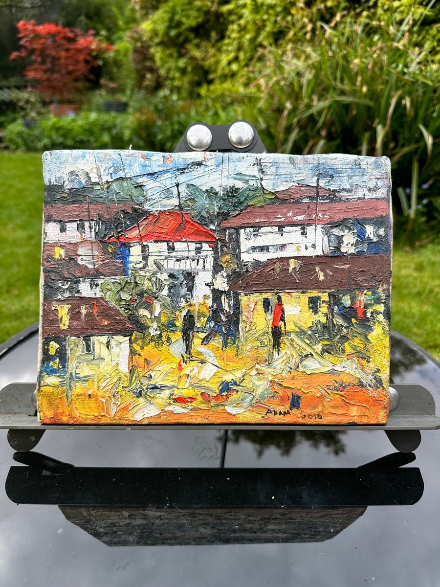 Displayed on an easel, Adam's "Lagos Streets" is a heavily textured miniature acrylic on canvas painting featuring houses with red and brown roofs, people walking, and lively yellow-green strokes—evoking garden charm.