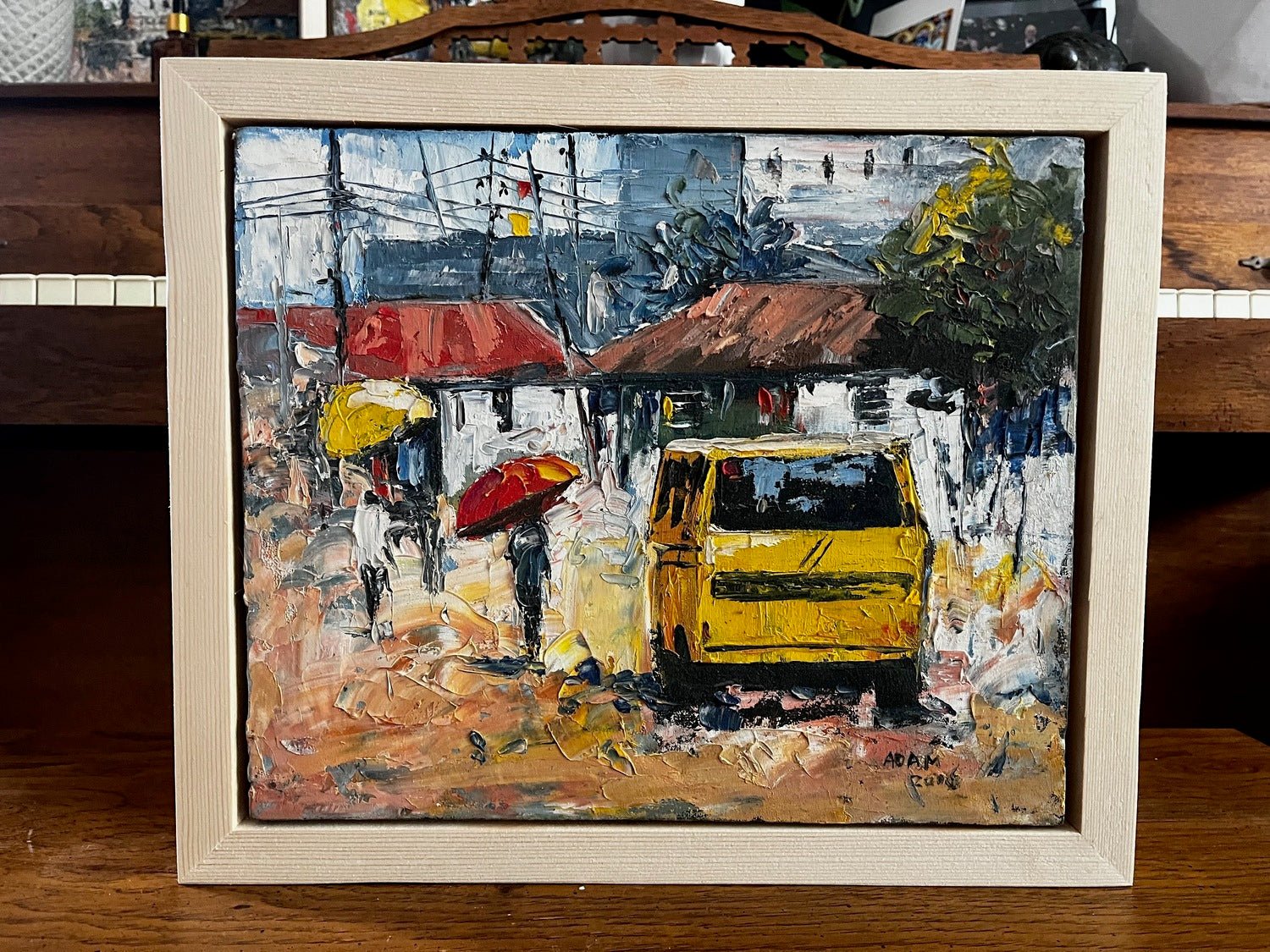 The Textured Miniature Painting by Adam depicts an impressionistic street scene with umbrella-carrying figures, a yellow vehicle, and red-roofed buildings. This bold acrylic-on-canvas piece comes with a certificate of authenticity.
