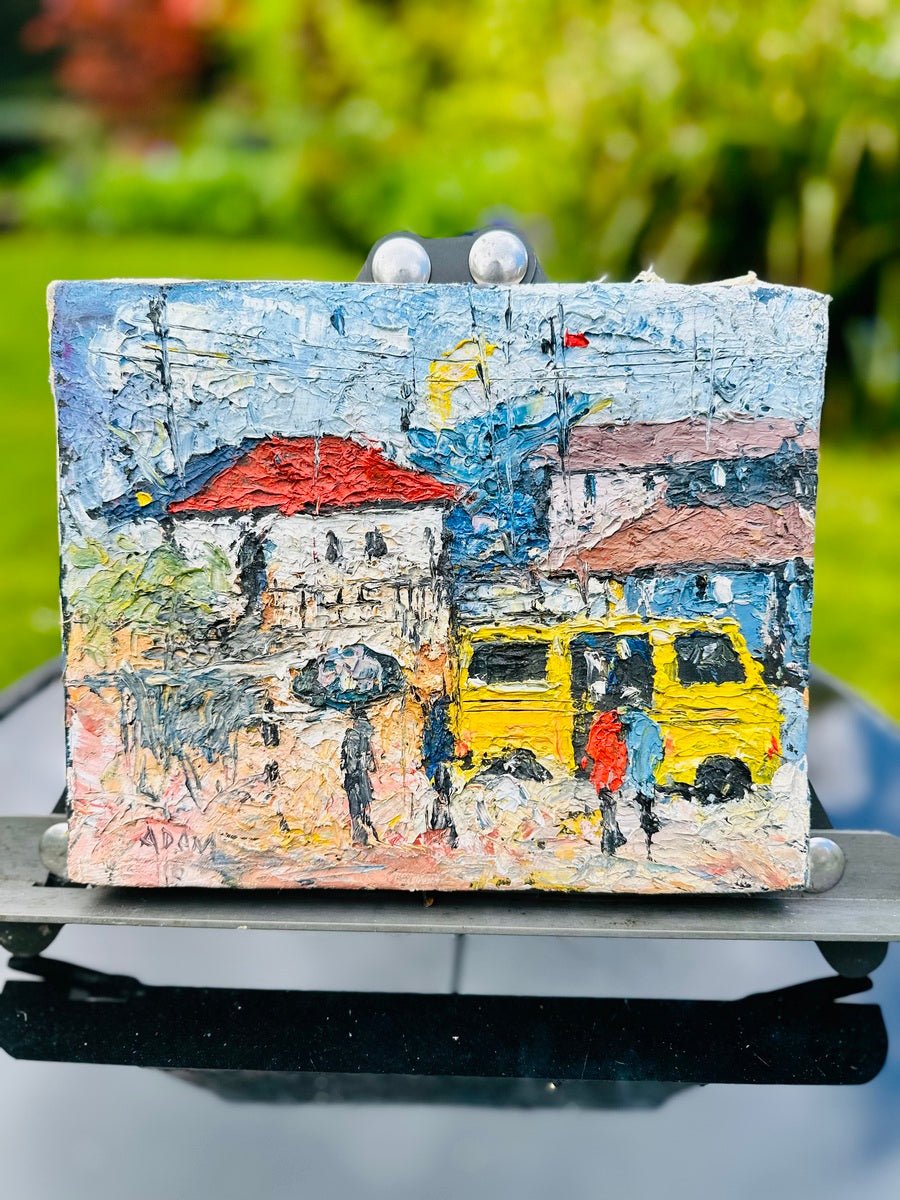 Heavily Textured Miniature Acrylic On Canvas Painting by Adam, 'Danfo Bus': A vivid Nigerian street scene with people, a bright yellow bus, red and brown roofed buildings, and green trees, displayed outdoors on a stand.