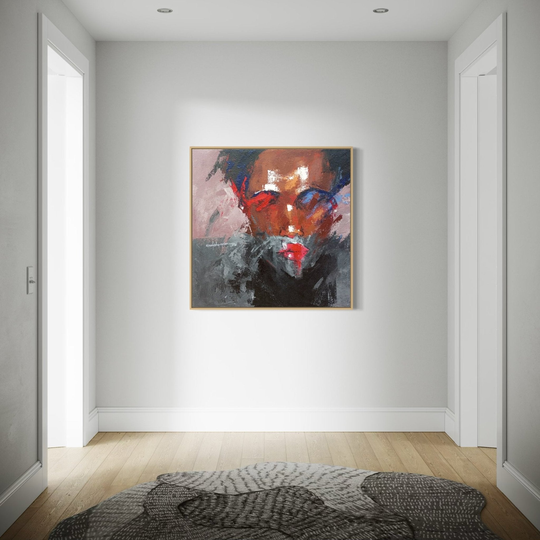 A modern hallway with light wood floors and white walls features "Where I Am" (93 x 93cm) by Olasunkanmi Oyelusi, an abstract acrylic on canvas depicting a bold face, displayed above a gray patterned rug.