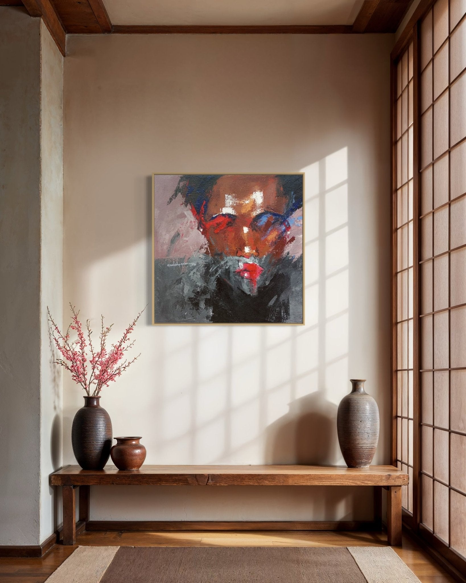 A minimalist room with wooden accents features a bench with pottery and pink blossoms. Above, "Where I Am" (93 x 93cm) by Olasunkanmi Oyelusi adds vibrant red and dark tones as sunlight casts shadows across the wall and floor.
