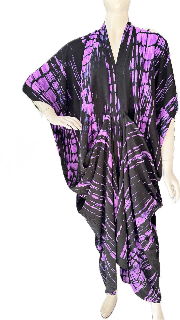 A mannequin showcases the Zoya Drapped Dress by bibianna.co.uk, a loose kaftan midi featuring bold purple tie-dye on black, wide sleeves, and an asymmetrical hem for a flowing, elegant style.