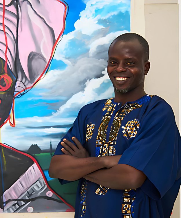 Artist oyelusi smiling standing in front of his artwork large blue cloud like background