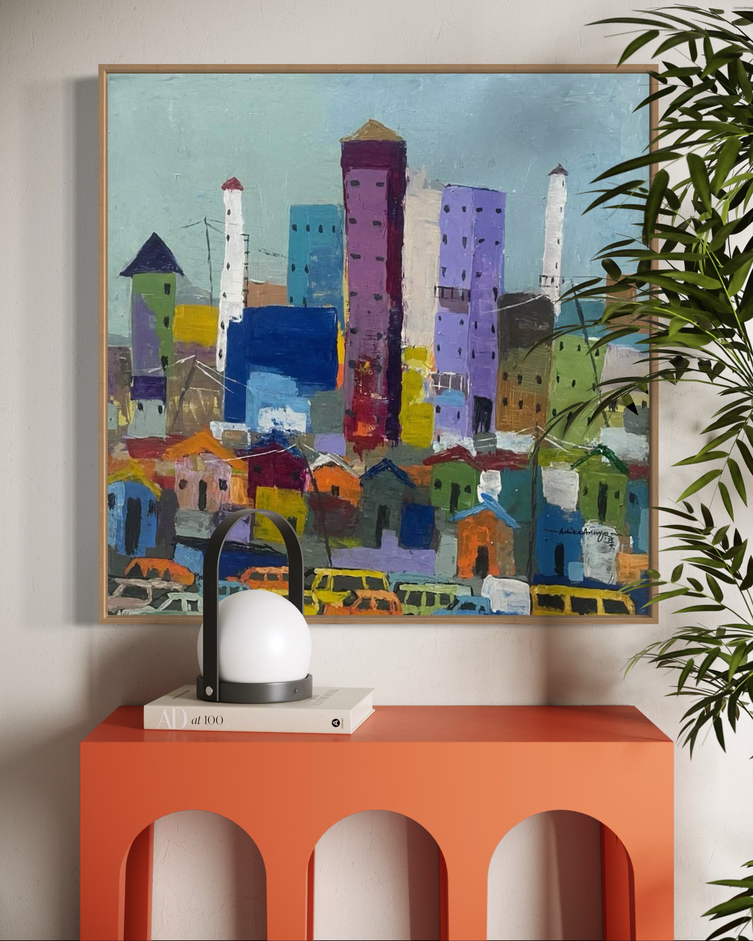 Somewhere In Lagos City," a hand-signed abstract cityscape by Achike Anayo, hangs above an orange console table with a lantern-style lamp, white book, and leafy plant. Includes certificate of authenticity.