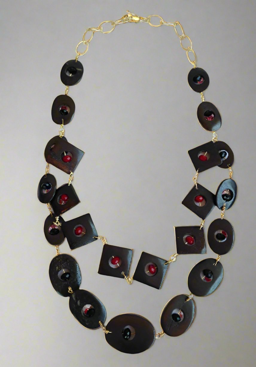 The Ariaba Wood and Crystal Tiered Necklace from bibianna.co.uk features alternating oval and square black beads with red centers, all linked by a 14k gold-plated wire chain and finished with a gold clasp.
