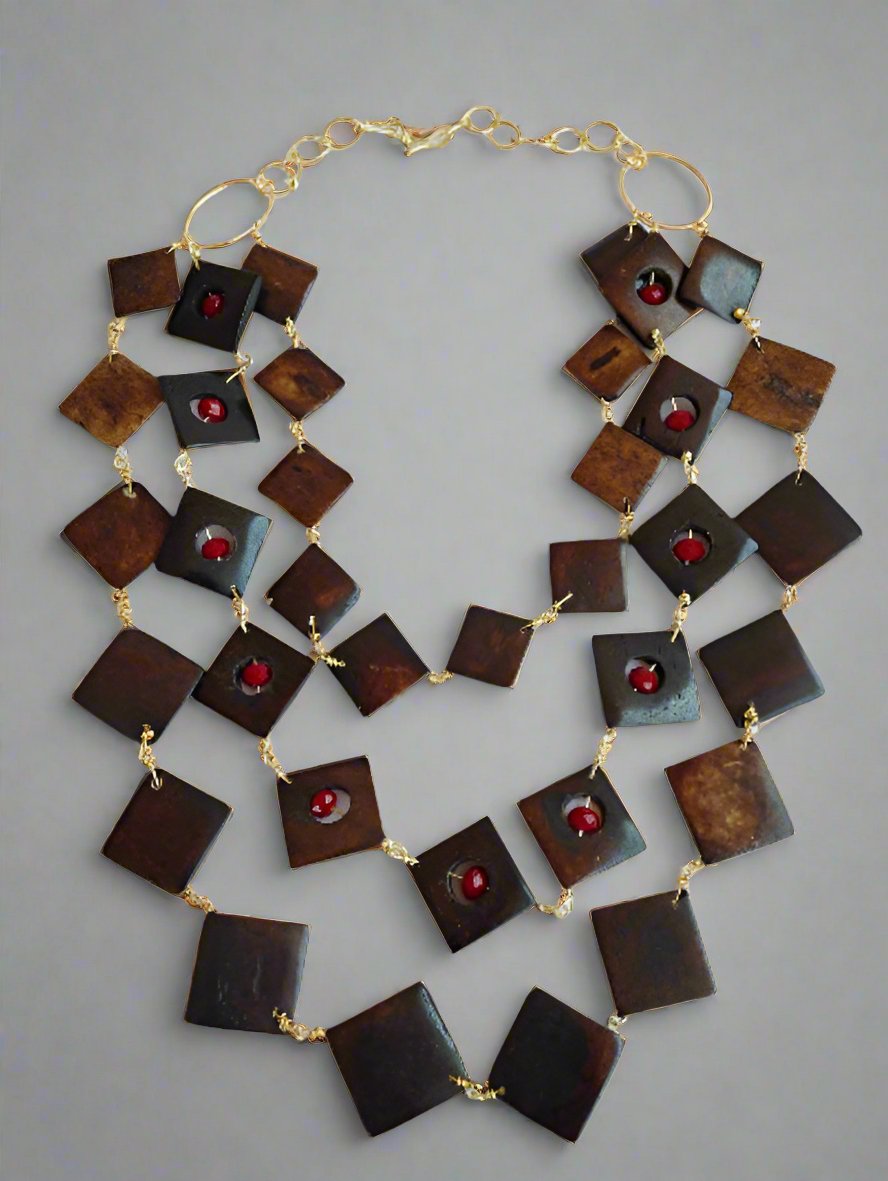 The Ariaba Wood and Crystal Tiered Necklace by bibianna.co.uk features three strands of large square dark brown beads, small red round accents, and a 14k gold plated wire chain link with a gold clasp.