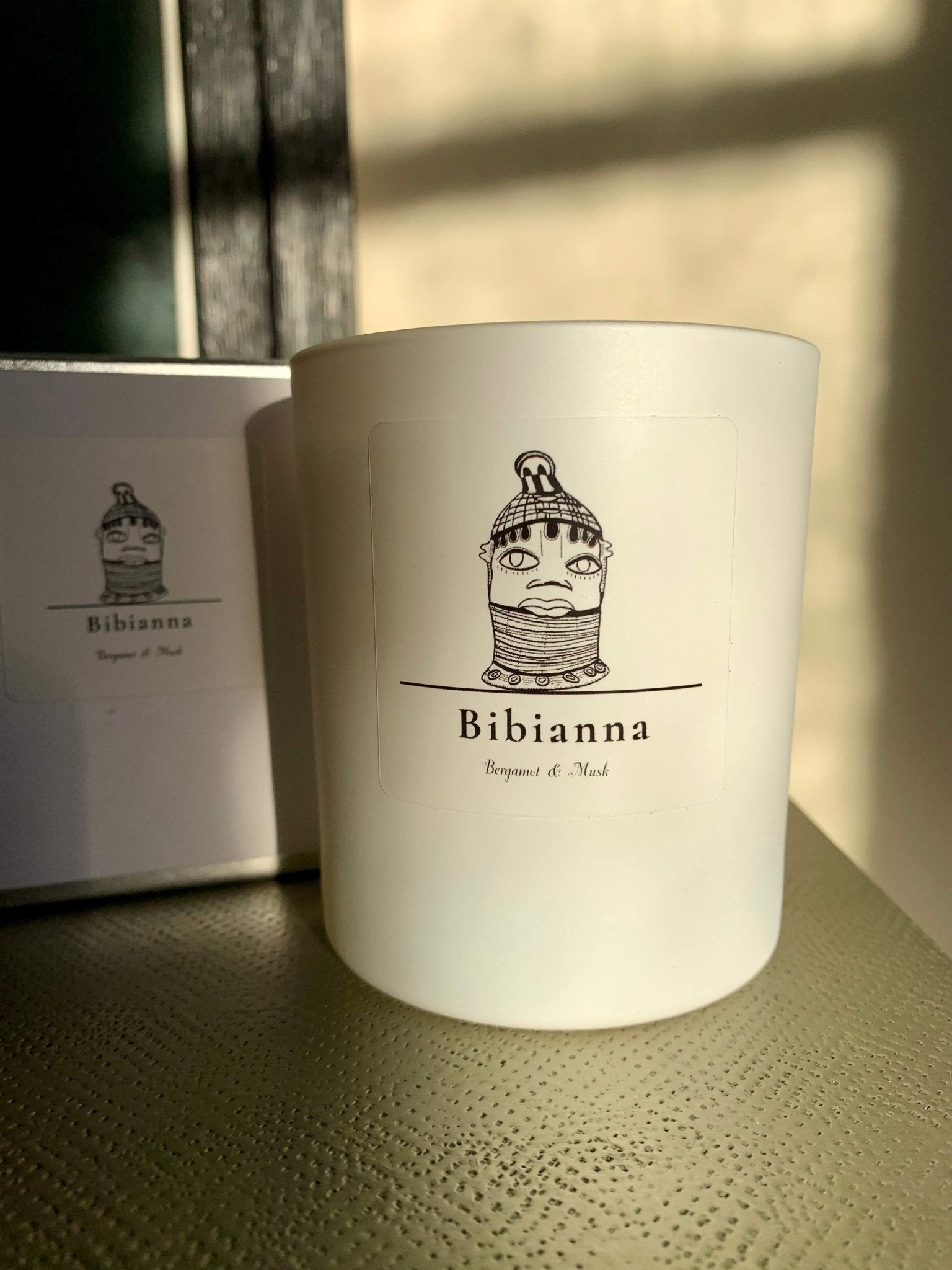 Sip your favorite brew from a white mug with a logo while enjoying the bibianna.co.uk Bibianna Visual Scented Candle – Bergamot & Musk for a touch of luxury.