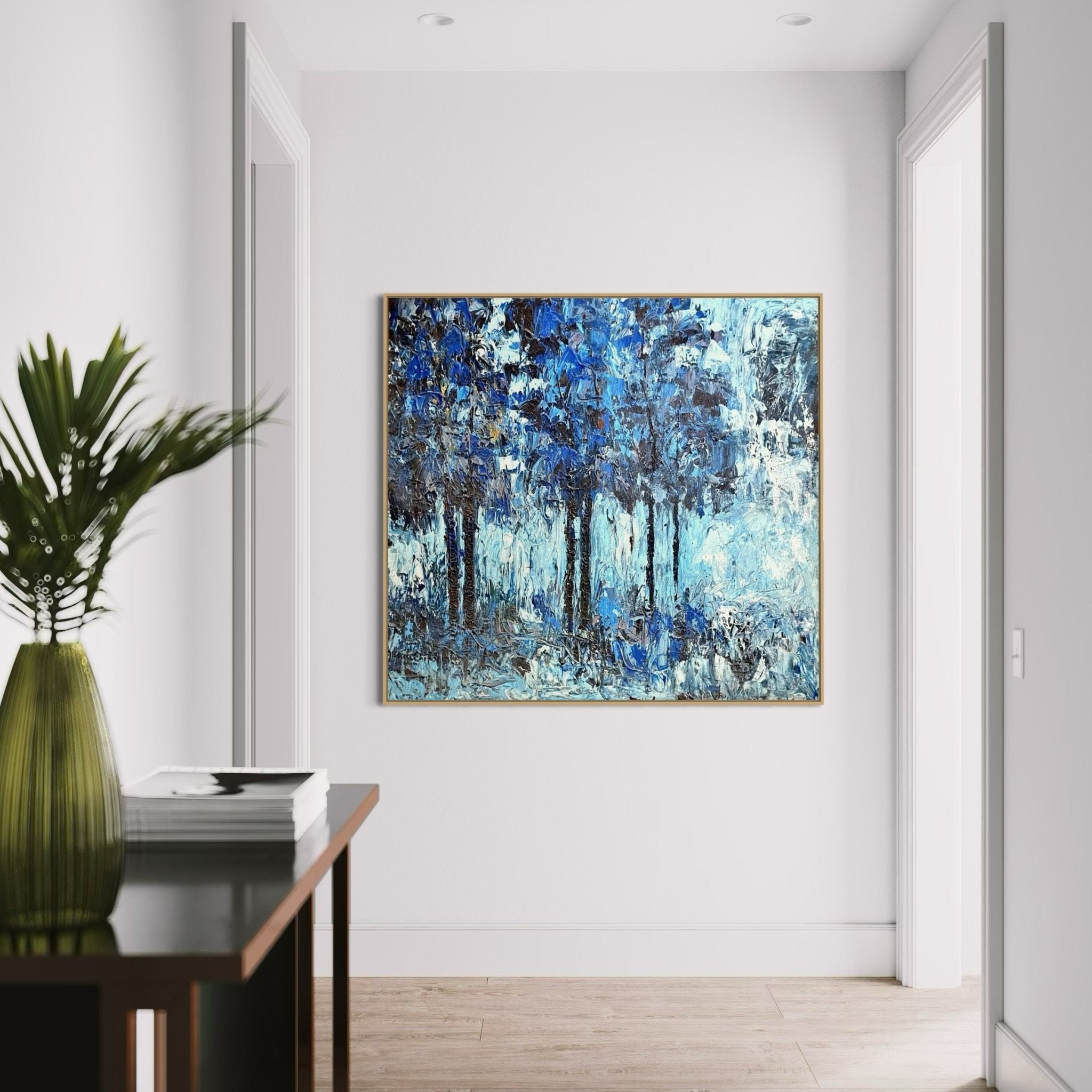 A modern hallway with light walls and wood floors showcases Akhile Ehiforia's Extra Large Textured Impasto Nature Painting, "Growth Series," plus a dark table on the left with a green vase and leafy plant.
