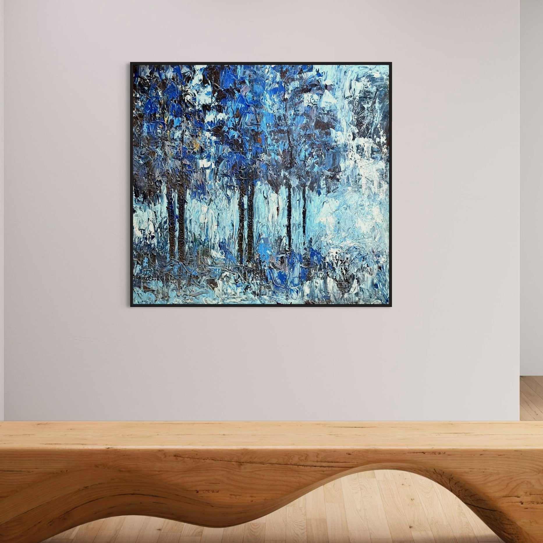 The "Growth Series" Extra Large Textured Impasto Nature Painting by Akhile Ehiforia features abstract blue and white tones, resembling a forest, and pairs beautifully above a sculpted wooden bench with a curved, wave-like design.