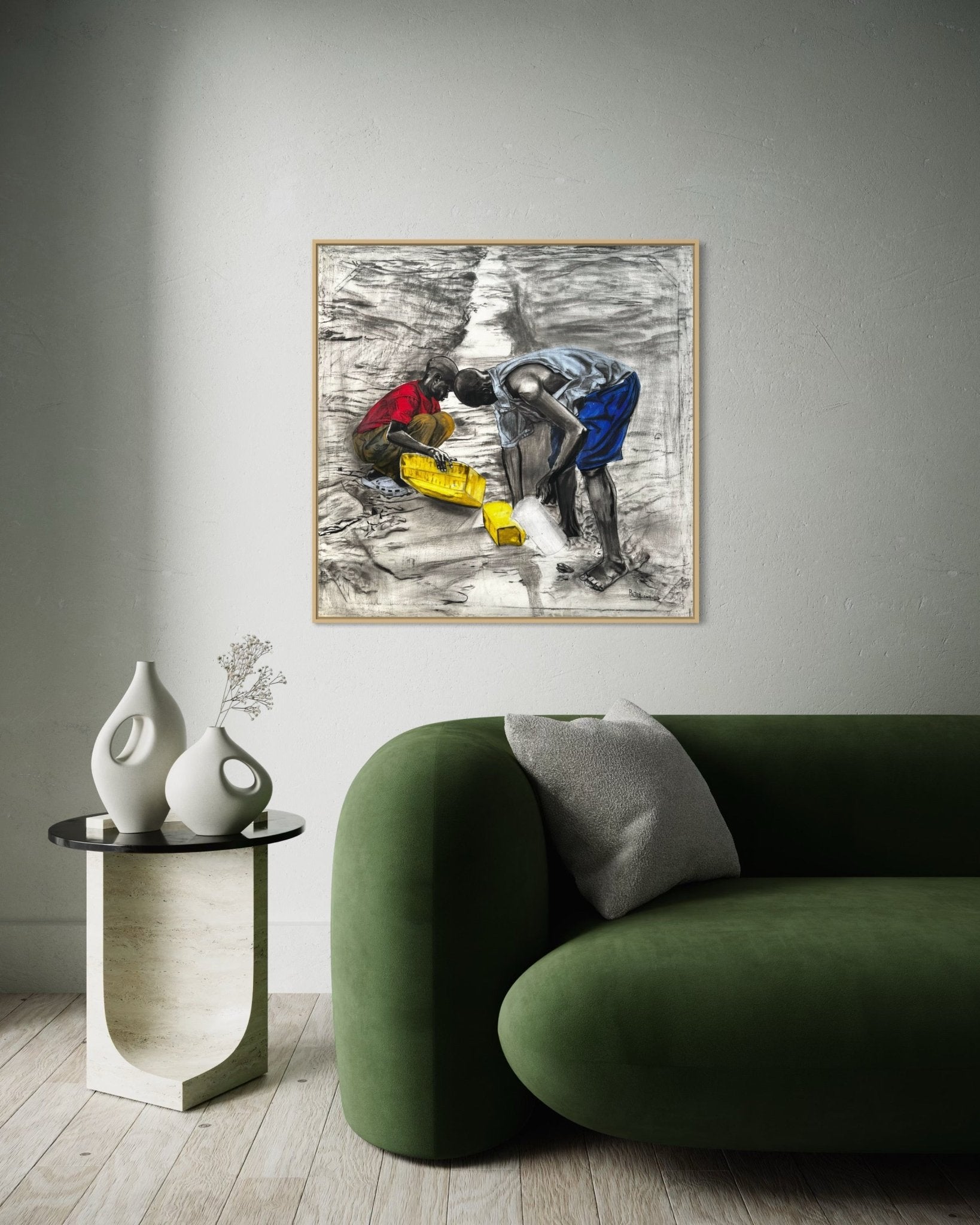 A modern living room features a green sofa, grey pillow, round side table with white vases, and "Fetching Water" by Bibianna African Art Collective—a framed painting of two figures collecting water—displayed above the sofa.