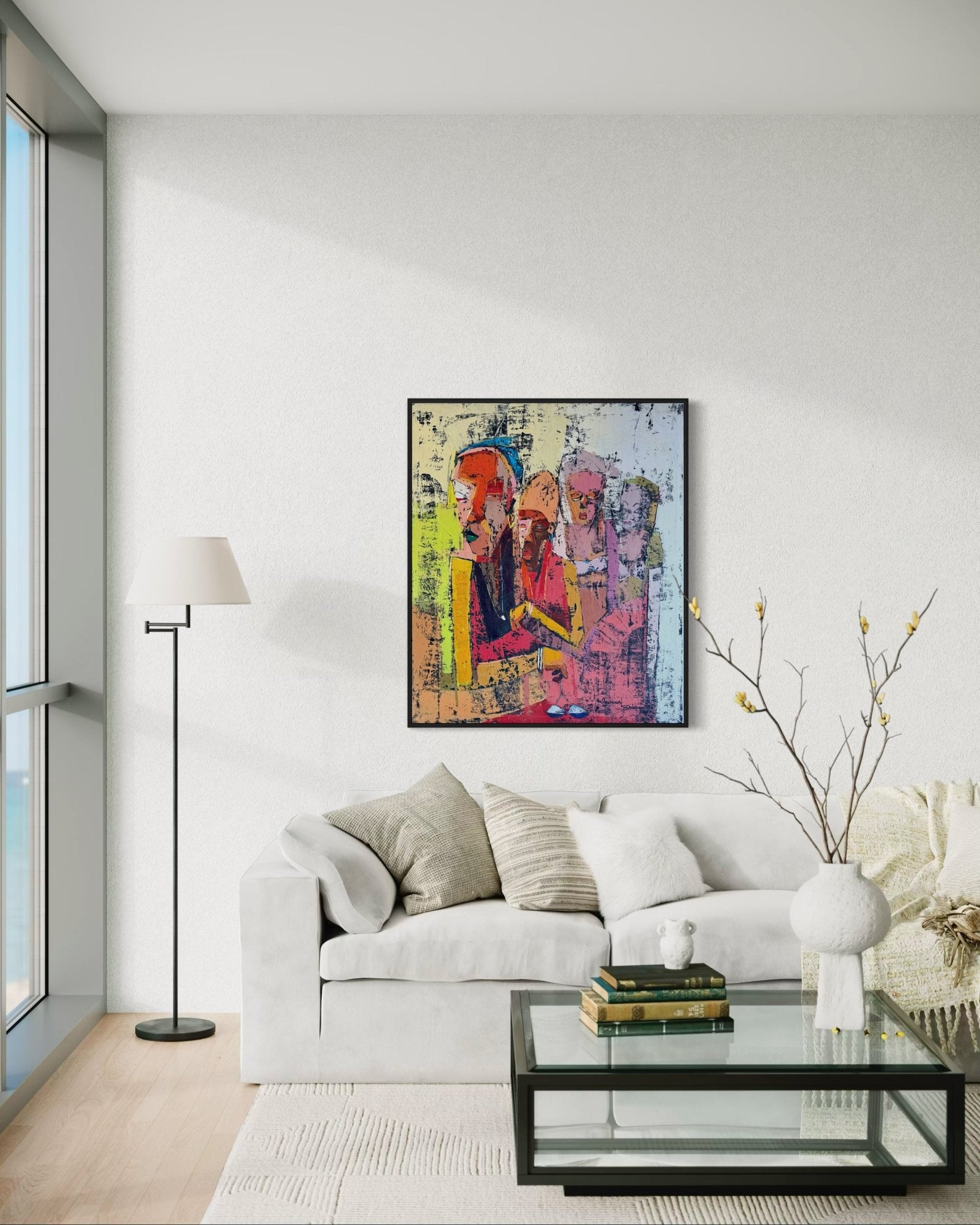 A modern living room with a white sofa, glass coffee table, and floor lamp. Above the sofa hangs 'Gender Equality' by Dolapo Ogunnusi—hand-signed and with a certificate of authenticity. Large windows fill the space with light; books decorate the table.
