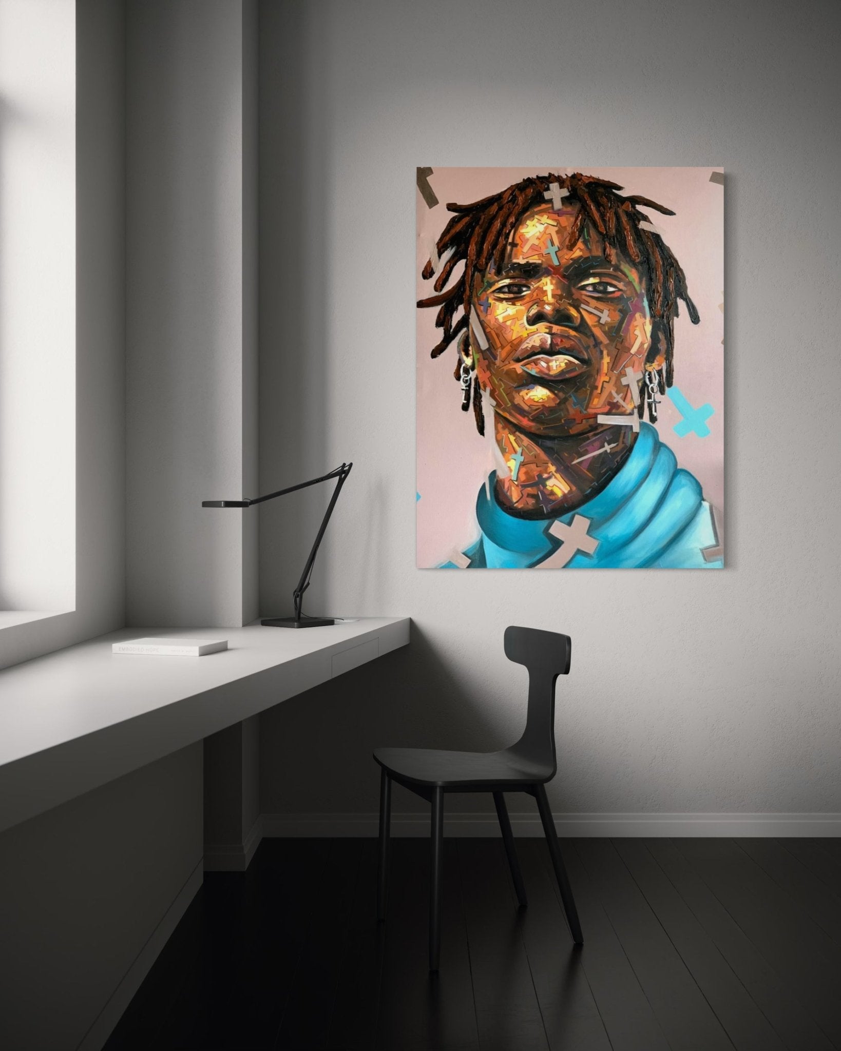 A minimalist 2024 room with a white desk and black chair. Above the chair, Agboola Emmanuel I’s ‘Manifest’ expressionist portrait by Emmanuel (Copy) depicts a dreadlocked figure breaking through limitation on the gray wall. Light enters from a large window.