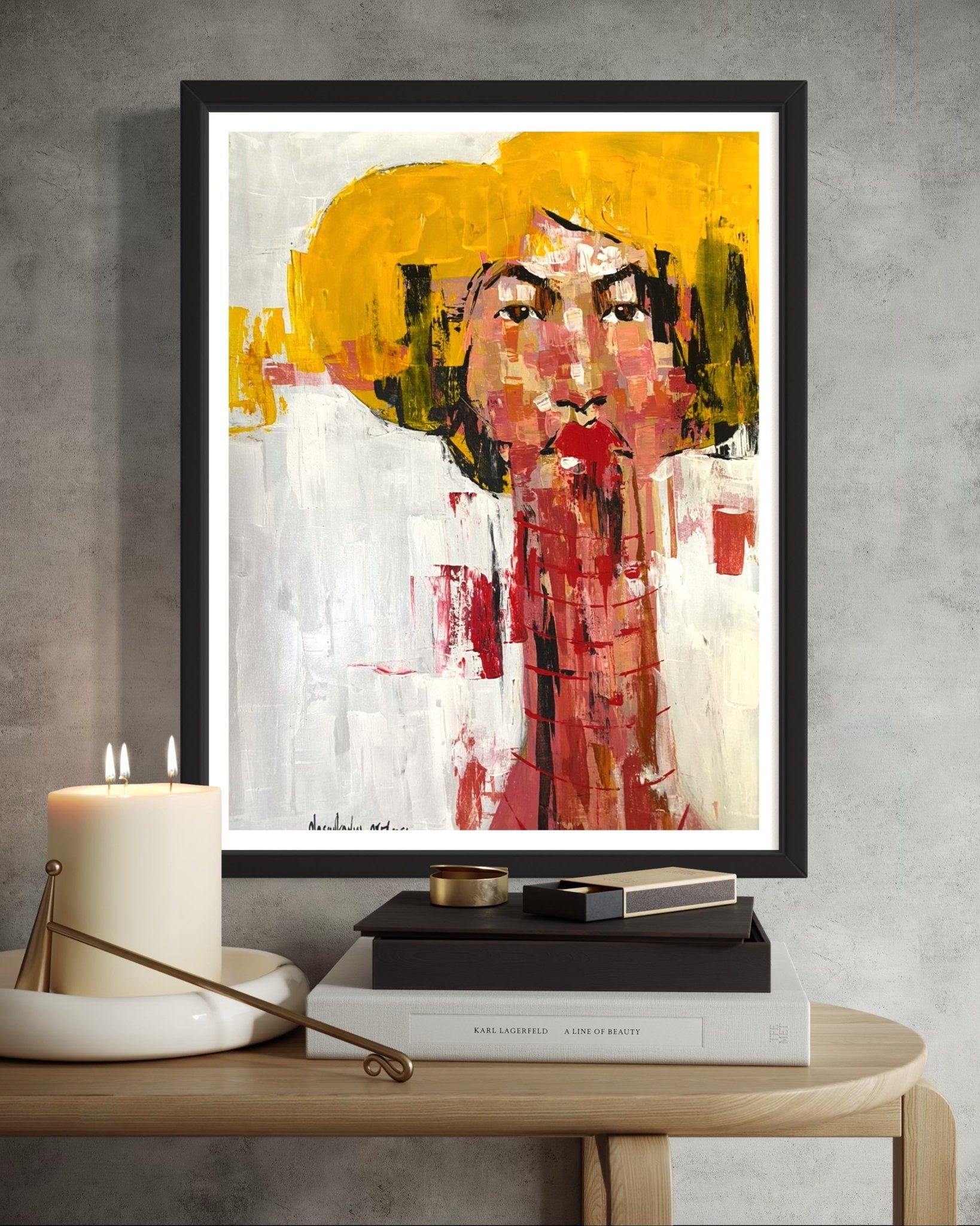 A framed "One of a Kind Series by Oyelusi" original by Olasunkanmi Oyelusi hangs above a table with candles and books. It depicts a woman in a yellow hat, painted with bold red, yellow, white, and black acrylic on paper.