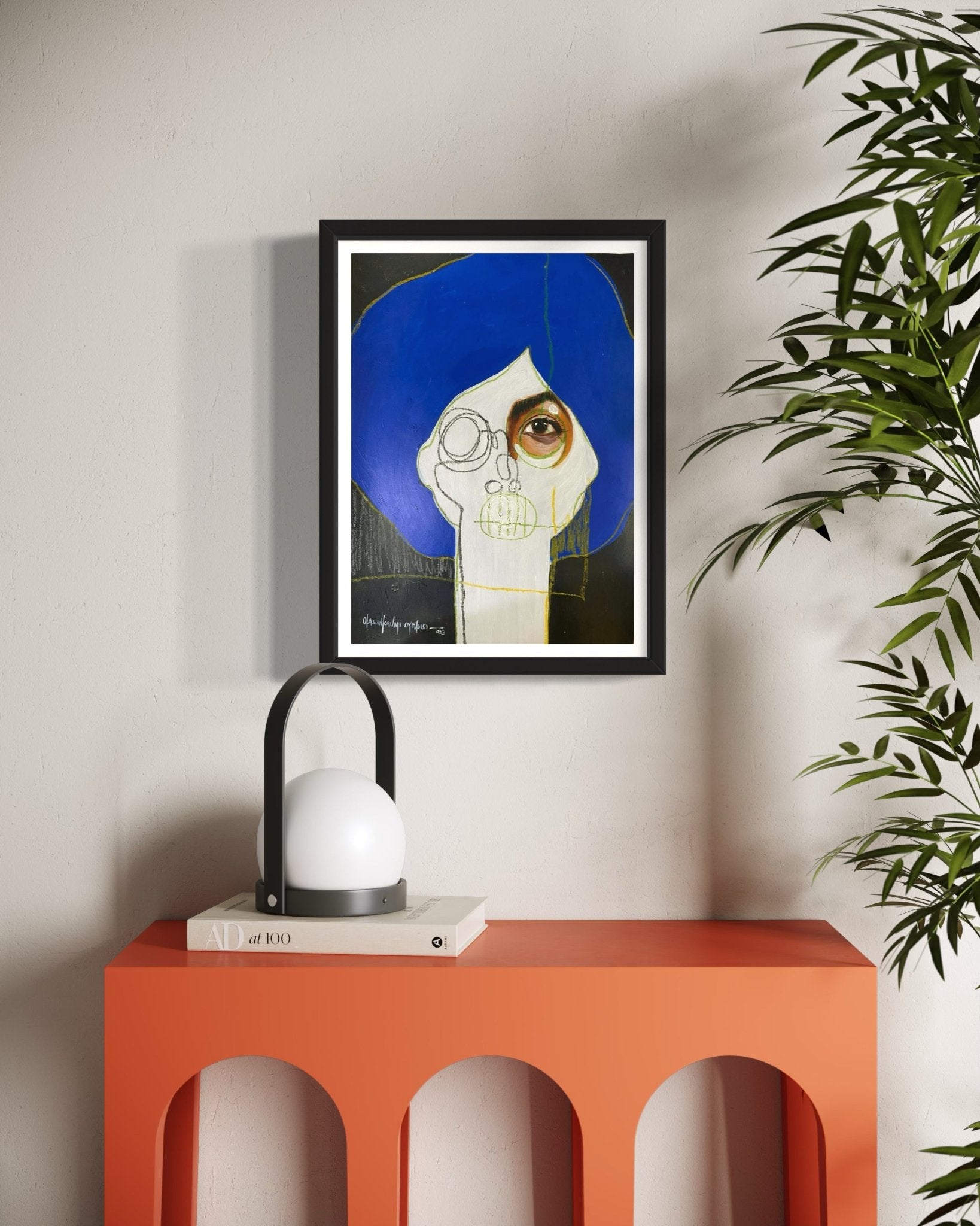 A modern interior features an orange console, round white lamp with books, a leafy plant, and "One of a Kind Series by Oyelusi" abstract portrait by Olasunkanmi Oyelusi with a blue headpiece framed on the wall.