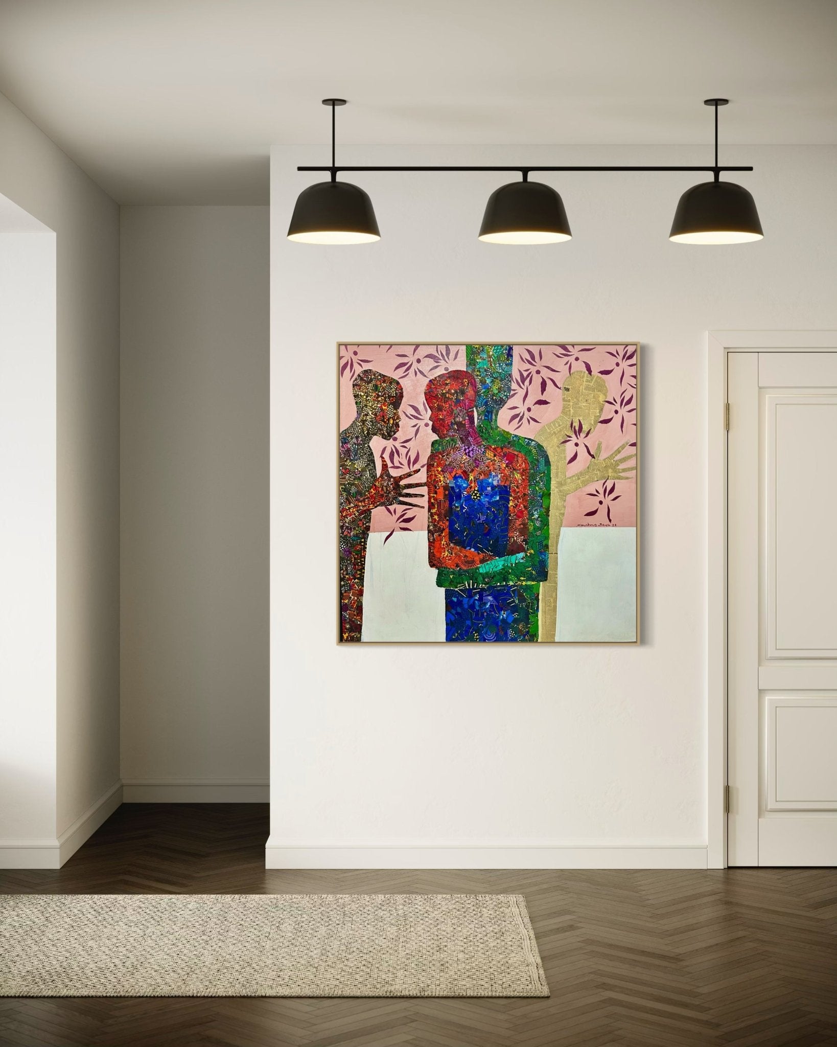 A modern hallway with dark wood floors and white walls features "Self" by Seye Morakinyo—a colorful abstract painting of two figures with floral patterns—illuminated by three black ceiling lights and displayed with a certificate of authenticity.