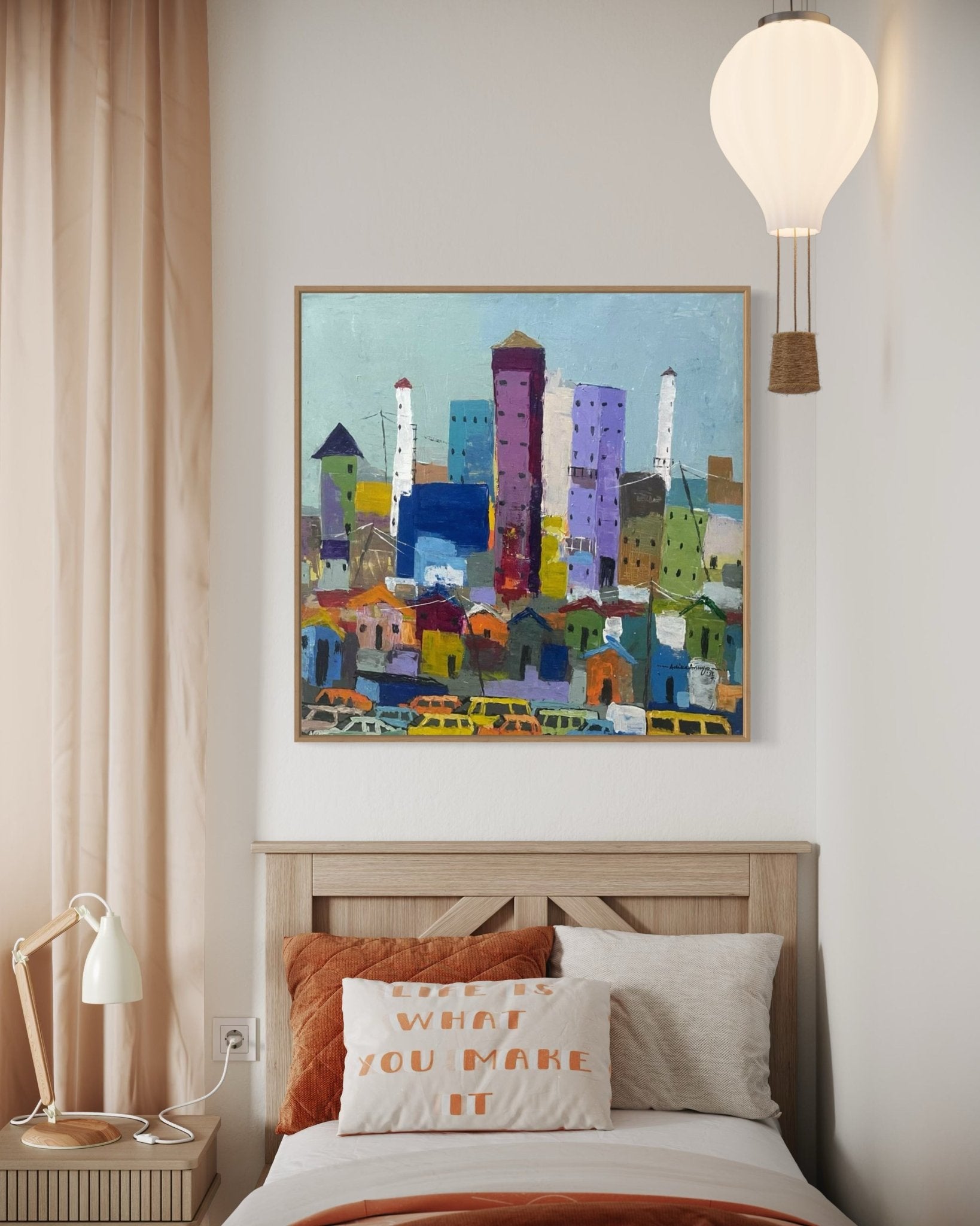 A cozy bedroom with a wooden bed, orange-and-white pillows, a reading lamp, and 'Somewhere In Lagos City' by Achike Anayo above the headboard. A white lantern-style ceiling light hangs overhead.