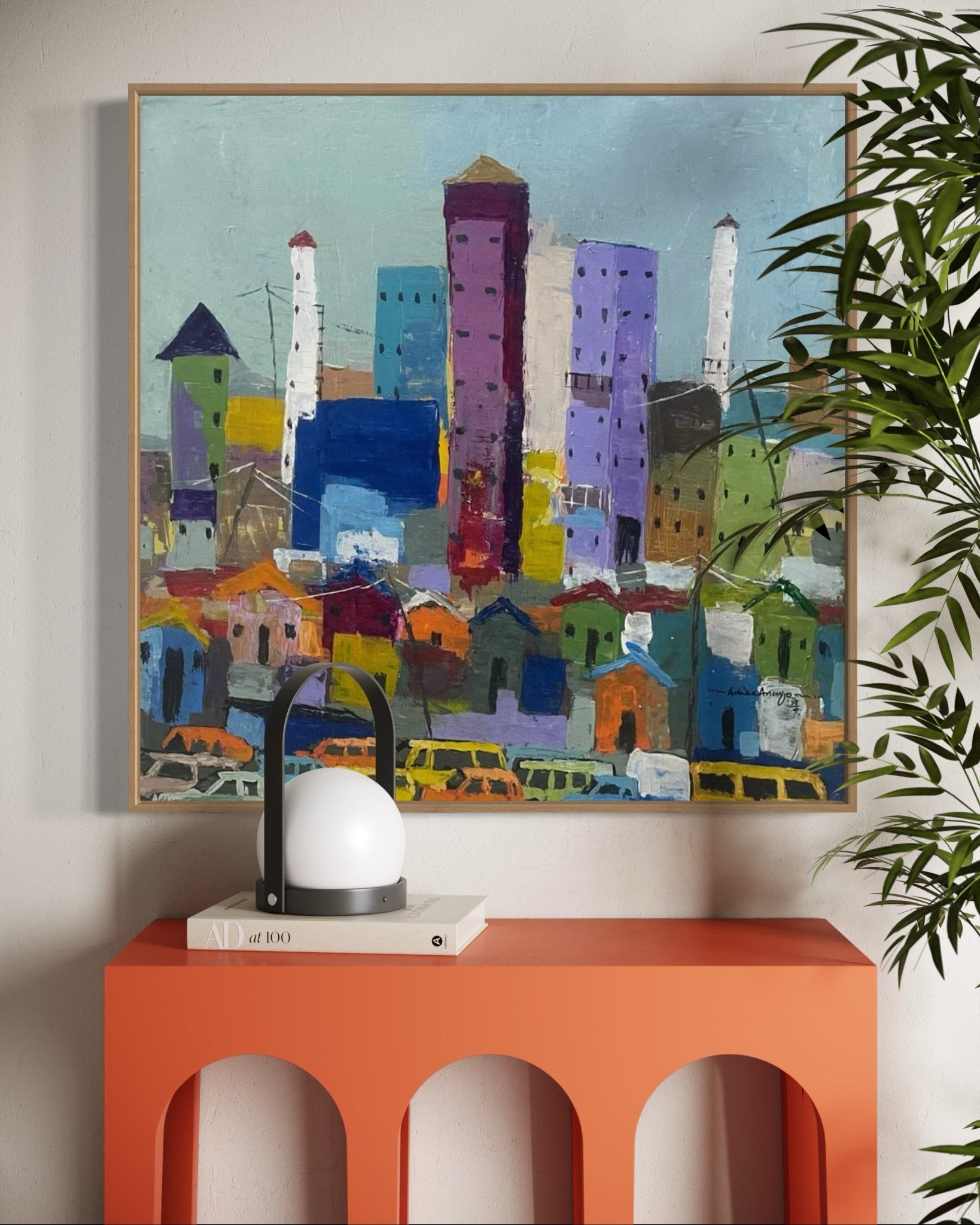 Somewhere In Lagos City," a hand-signed abstract cityscape by Achike Anayo, hangs above an orange console table with a lantern-style lamp, white book, and leafy plant. Includes certificate of authenticity.