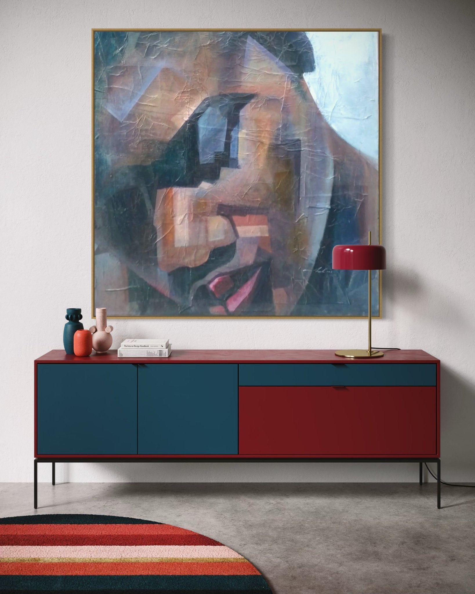 A modern room with a red and blue sideboard, red table lamp, decorative vases, and "Peace" Textured Painting by Christopher Ankeli—an abstract acrylic portrait—hanging above. A colorful striped rug enlivens the floor.