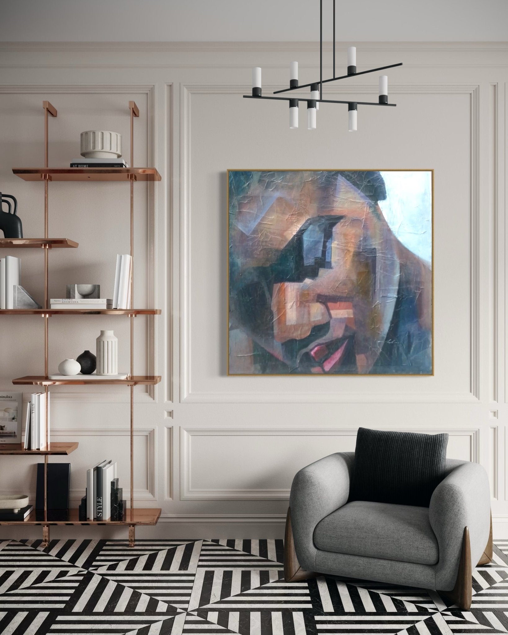 Modern living room with geometric black-and-white rug, gray armchair, copper bookshelves, and "Peace" Textured Painting by Christopher Ankeli—an abstract face acrylic—displayed on a light-paneled wall beneath a black chandelier.