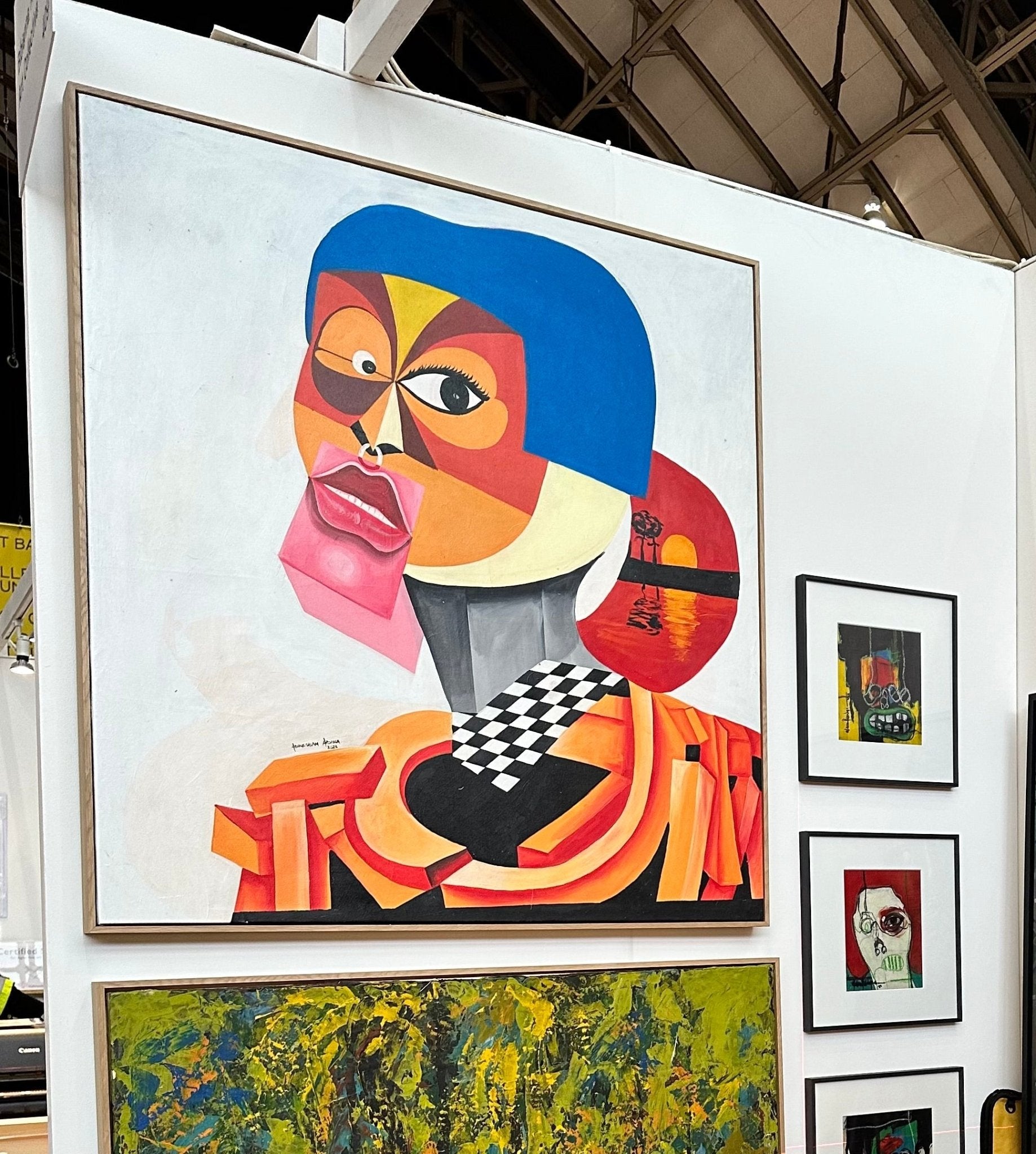 “Tranquil Night” (126 x 120cm) by Abiola Abdulsalam—a vibrant abstract portrait with cubist influences and bold colors—hangs in a gallery among modern works, including a green-yellow abstract and smaller framed portraits.