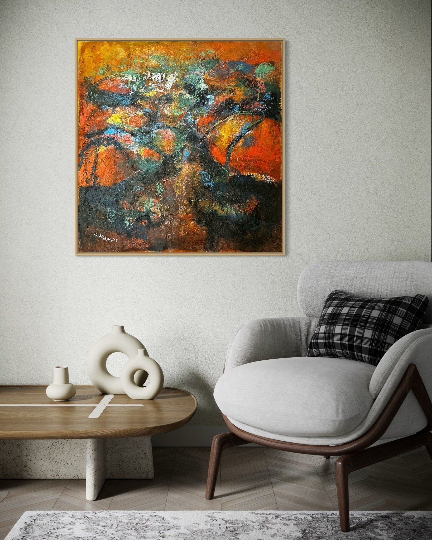 A modern living room with a gray armchair, plaid pillow, stylish coffee table with abstract white vases, and “Tree Of Life” by Bibianna African Art Collective—hand-signed and featuring vibrant orange, green, and blue—on a light wall.