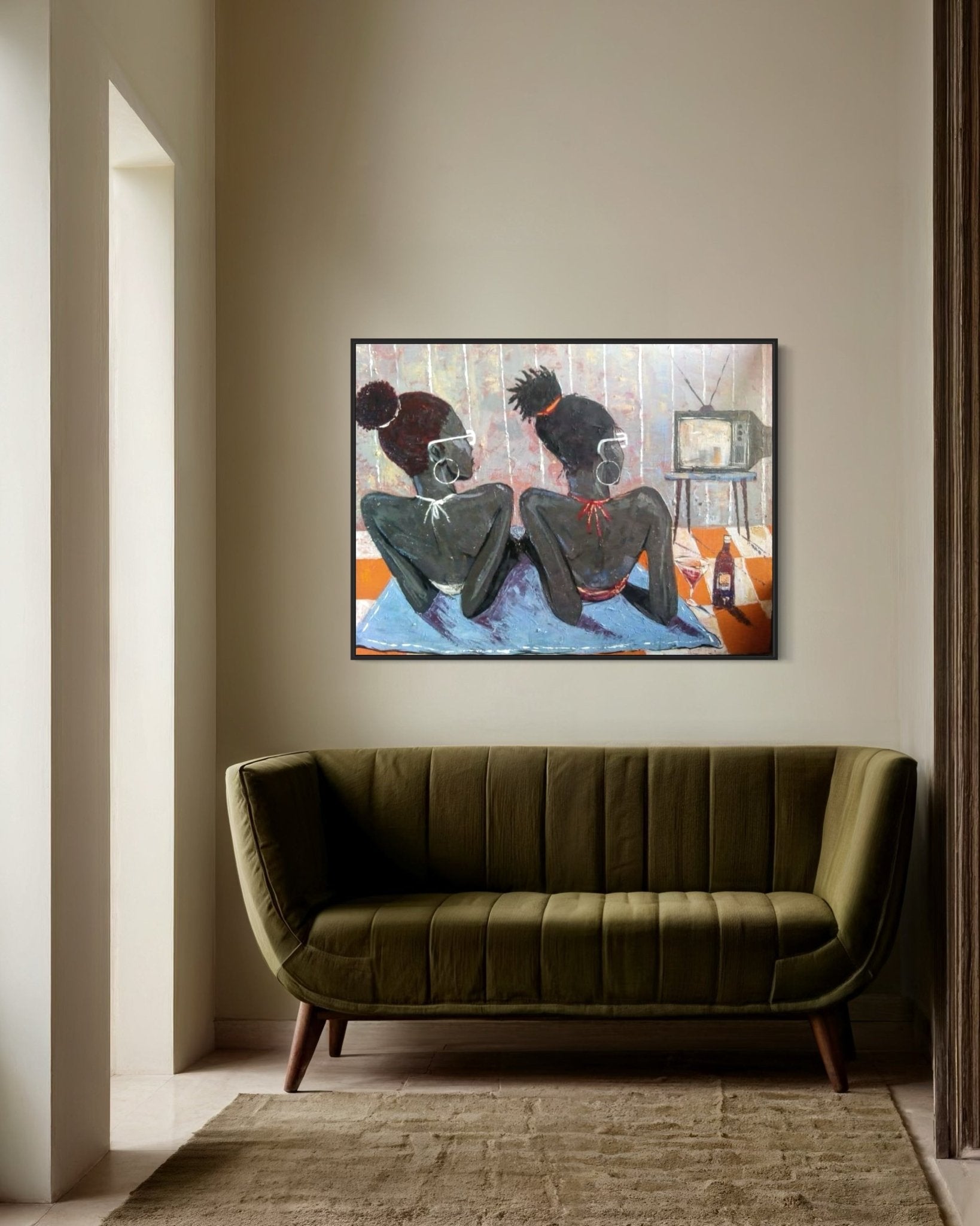 A modern living room with beige walls and a green velvet sofa features "Tween Vacation" by Lucky Isaiah, a hand-signed artwork of two figures with an old TV and bottle, above the sofa. A certificate of authenticity is included. Light streams through a tall doorway.